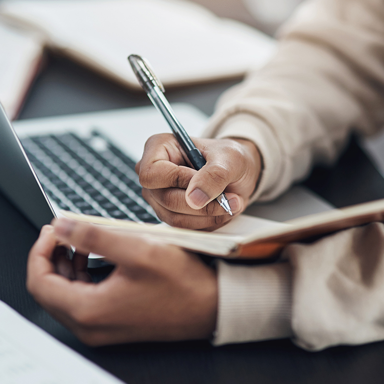 woman writing in a notebook by her computer