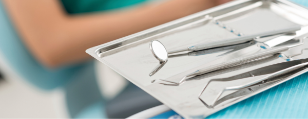 Dental instruments on a tray with a patient in the background.