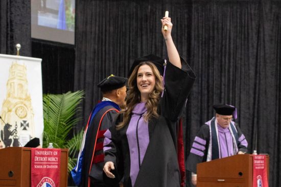 Female graduate holding up a diploma while walking across stage.